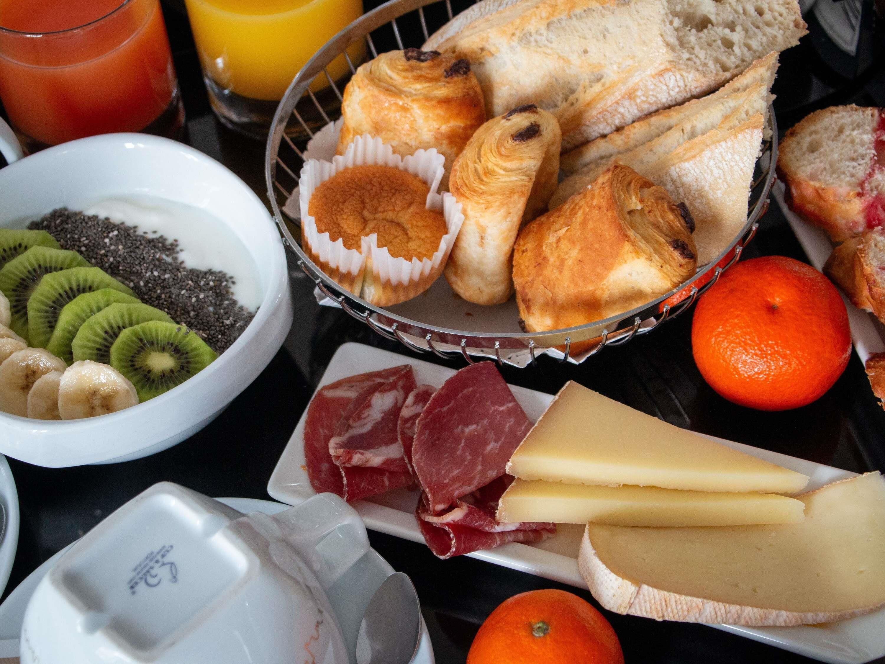 Una mesa con pan, bollería, queso y fruta.