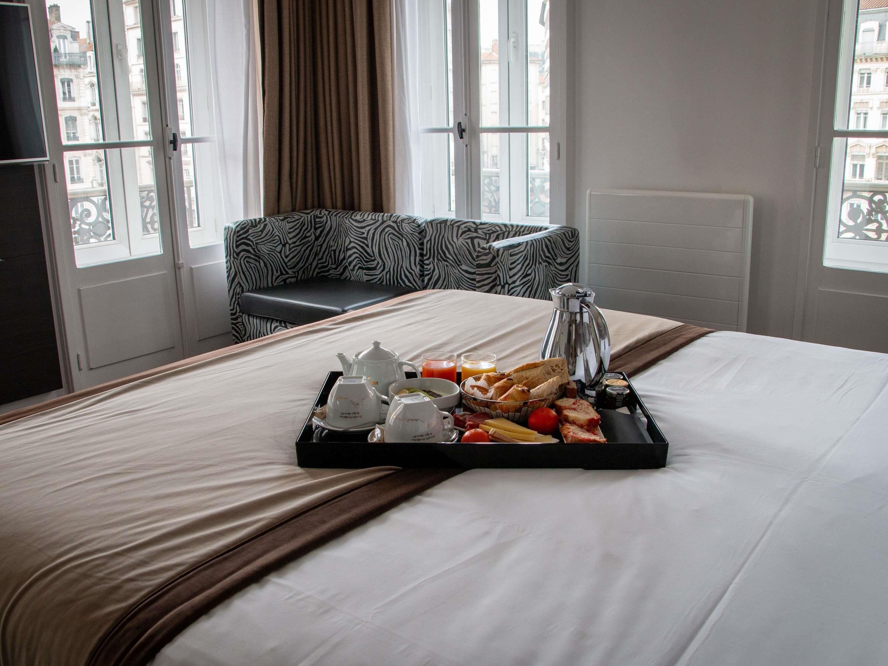 Ein Hotelzimmer mit einem Bett, einem Frühstücksbrett, einer Kaffeemaschine und Blick auf Gebäude durch das Fenster.
