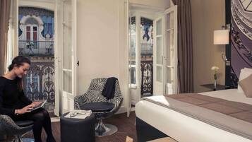 A hotel room with a bed, a chair, a small table, and an open door leading to a balcony.