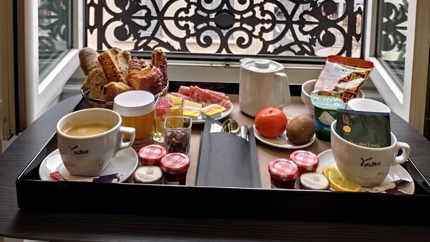 A breakfast tray with coffee, pastries, and a fruit on a balcony with a view of Parisian buildings. - Mercure Lyon Centre Beaux Arts (Lyon)