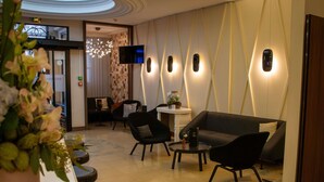 A lobby with a modern design, featuring a sofa, chairs, a small table, and a TV mounted on the wall. - Mercure Lyon Centre Beaux Arts (Lyon)