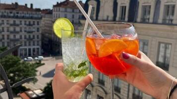 To cocktails med krebsegarn af lime og mynte, holdt i hænder med en bysilhuet og historiske bygninger i baggrunden.