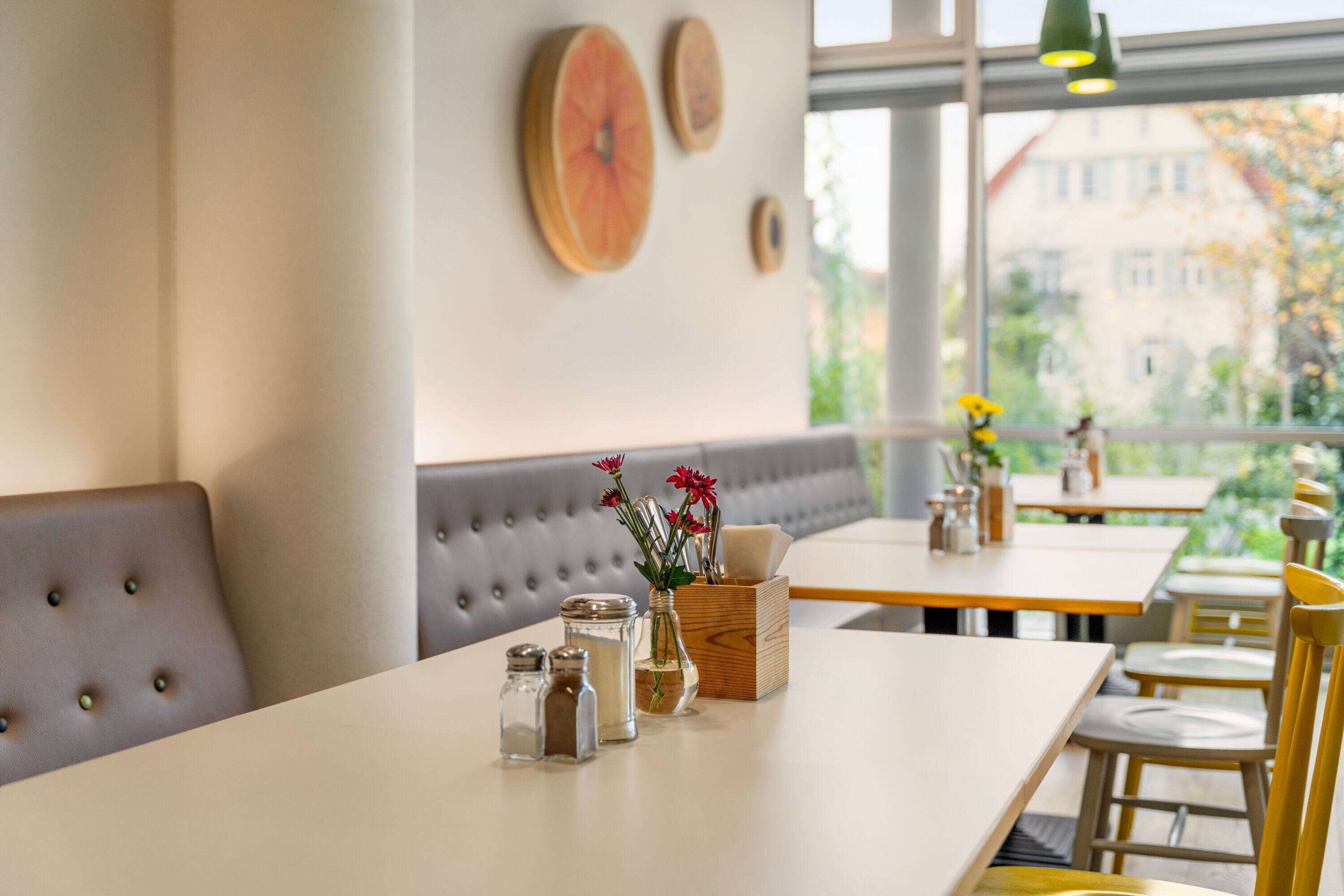 Een restaurantinterieur met een lange tafel, zachte zitplaatsen en uitzicht op buiten.