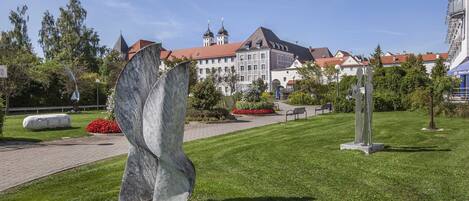 Une place publique avec une grande sculpture en marbre, un sentier et un bâtiment avec un toit rouge en arrière-plan.