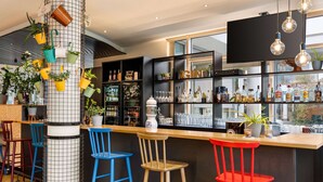 Un espace bar avec des tabourets, des étagères remplies de bouteilles et des plantes suspendues.