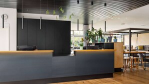 Un espace d’accueil moderne, doté d’un comptoir de réception sombre, d’un plancher en bois et de plantes en pot.