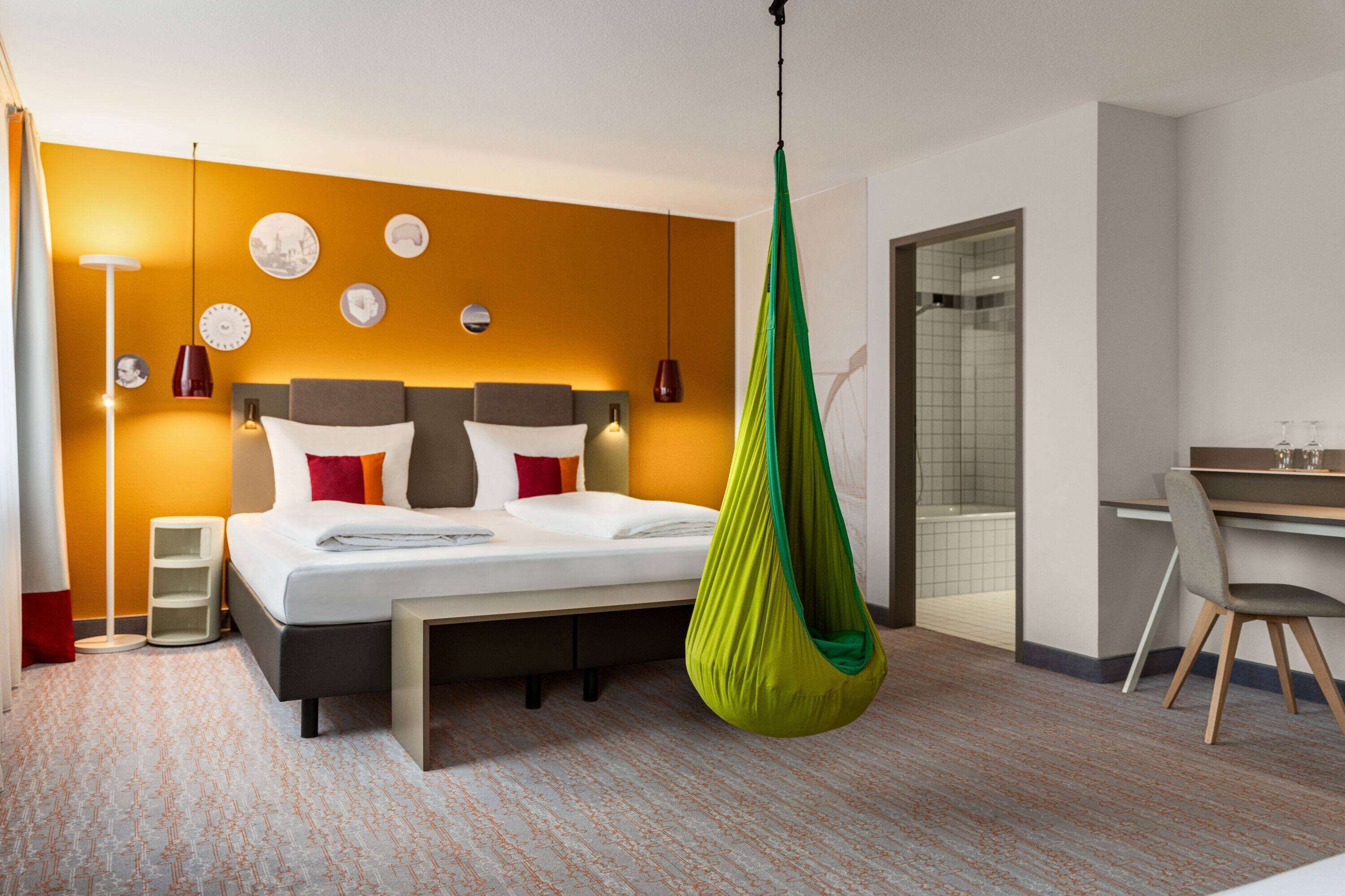 A modern hotel room with a bed, a desk, and a green hanging chair.