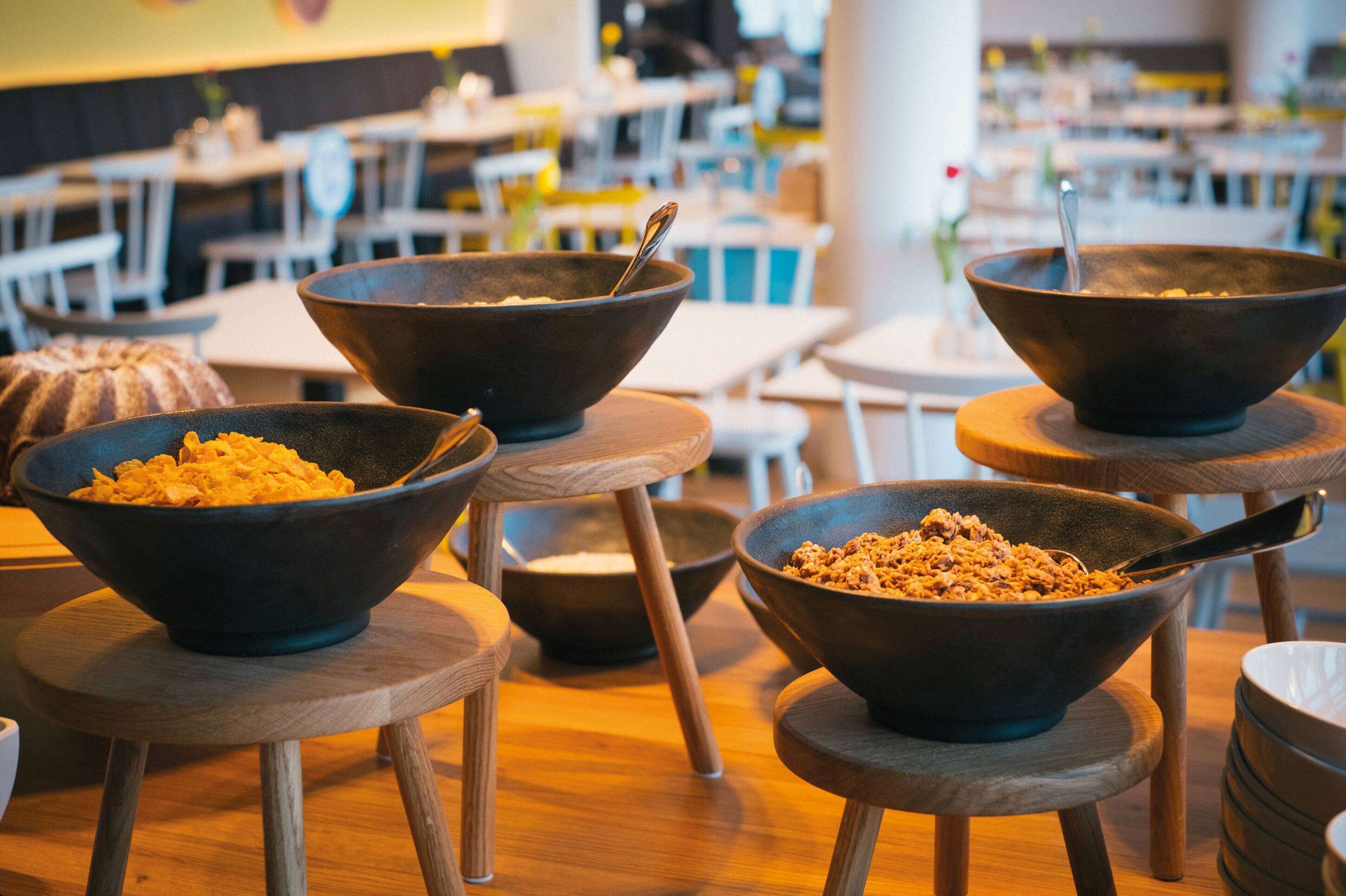 A dining area with multiple wooden tables and black bowls filled with food on wooden stools.