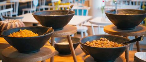 A dining area with multiple wooden tables and black bowls filled with food on wooden stools.