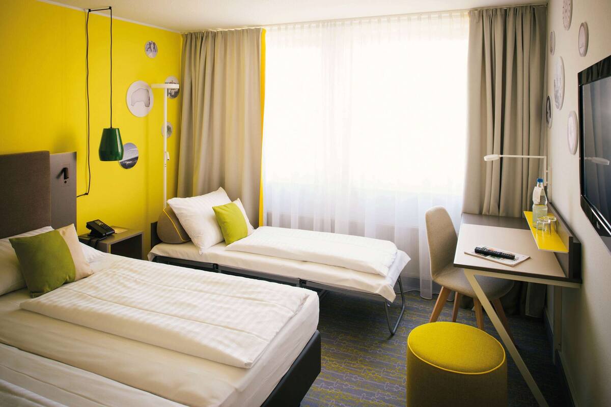 Een hotelkamer met twee bedden, een bureau, een stoel, een televisie en een raam met gordijnen.