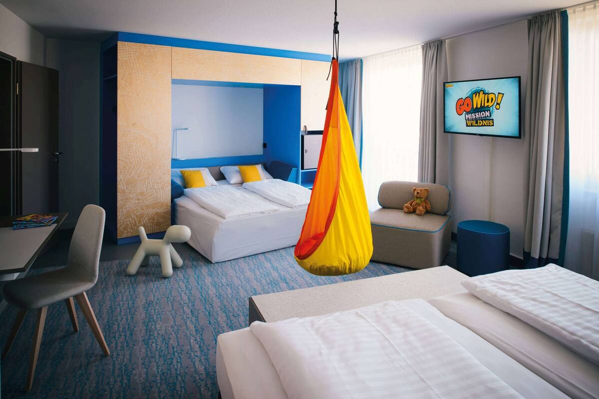 Hotelkamer met een bed, een bureau, een stoel, een hangstoel, een televisie en een teddybeer.