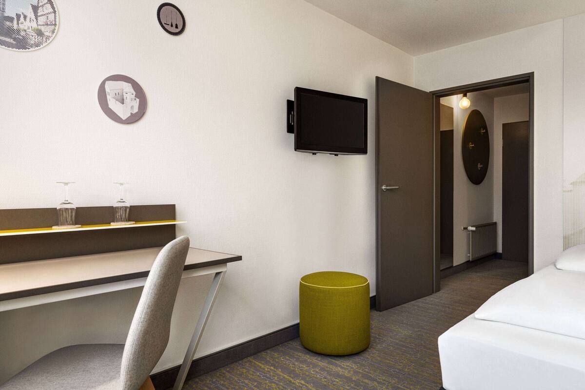 Een hotelkamer met een bed, een bureau met stoel, een televisie en een prullenbak.