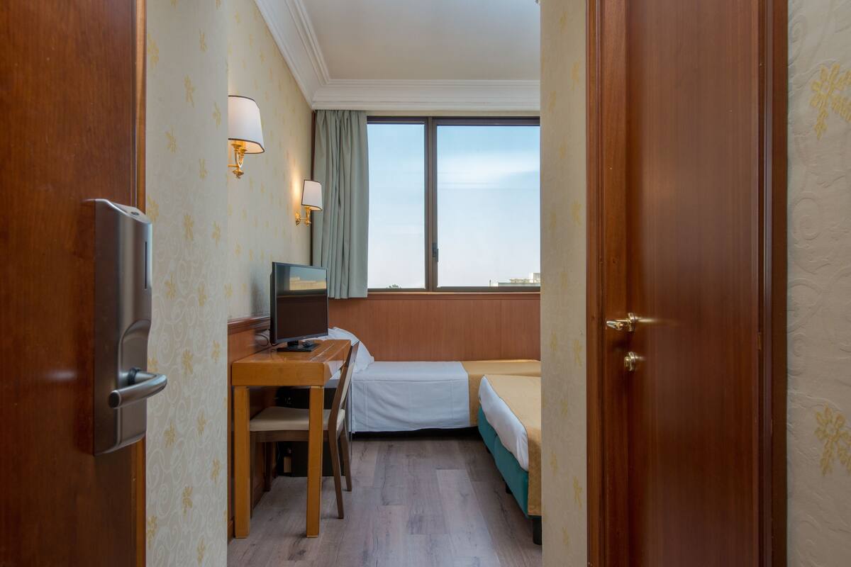 A hotel room with a wooden desk, a bed, a TV, and a window with a view.