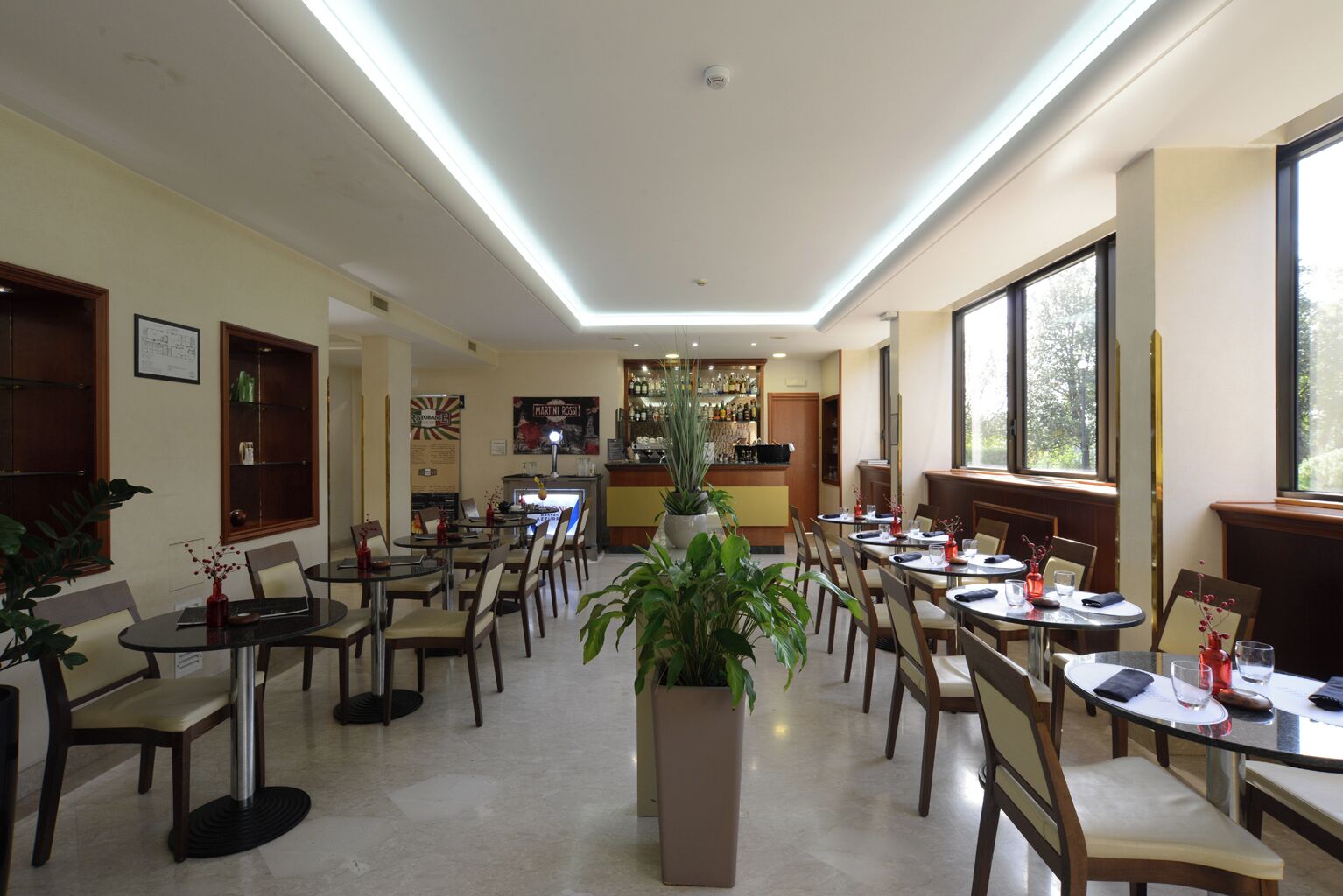 Un comedor amplio con varias mesas y sillas, una barra central, y grandes ventanales que dejan entrar luz natural.