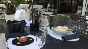 Una mesa de comedor con tártara de res, una ensalada, una copa de vino y una botella de vino.