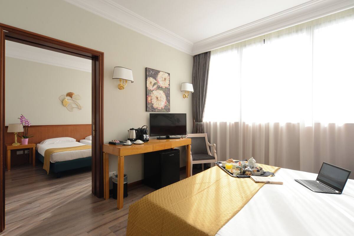 A hotel room with a bed, desk, chair, TV, and a laptop.