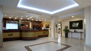 Zona de recepción de un hotel con diseño moderno, que cuenta con un mostrador de recepción, un reloj digital y un letrero en la pared.