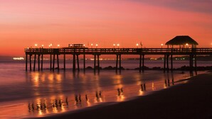 A pier extending into calm waters at sunset with lights along its length.