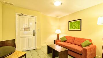 A room with a white door, a brown sofa with green cushions, a small table, and a lamp.