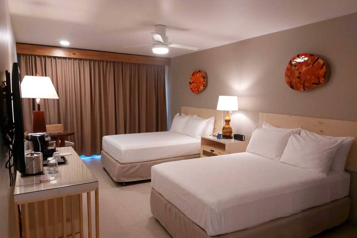 A hotel room with two beds, a desk with a lamp, a chair, and a curtain.
