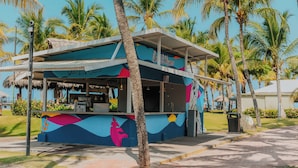 A colorful food kiosk with a tropical theme, surrounded by palm trees and a clear blue sky.