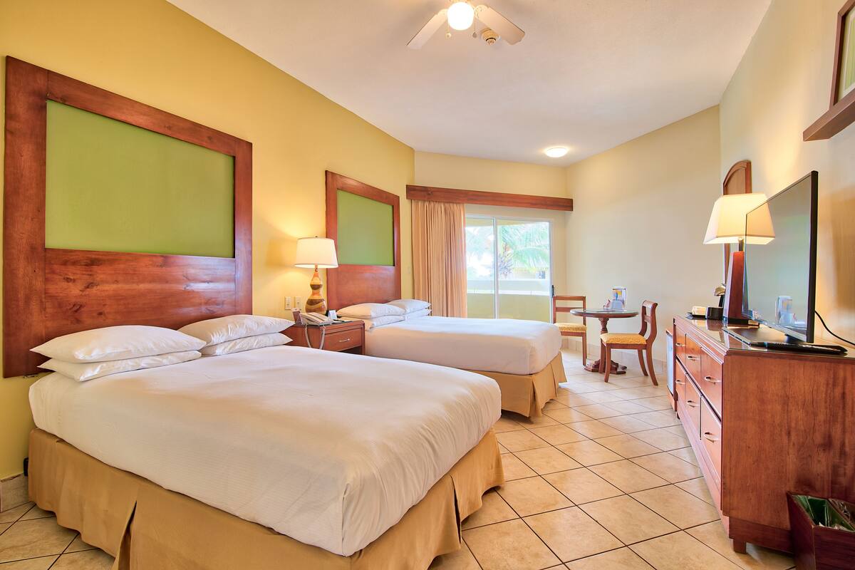 A hotel room with two beds, a desk, a chair, a TV, and a window.