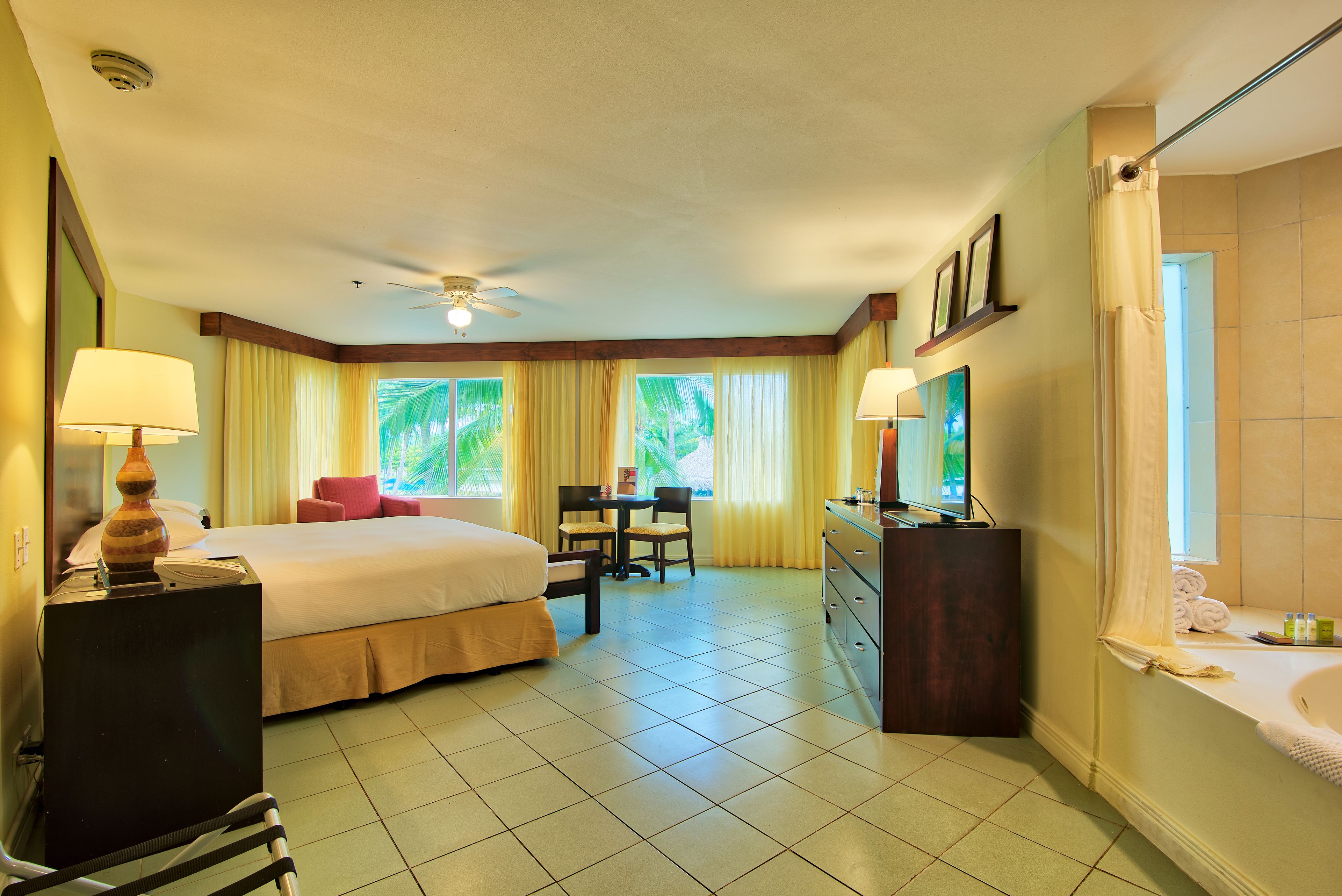 Quarto de hotel com cama, escrivaninha, cadeira e banheiro com banheira e pia.