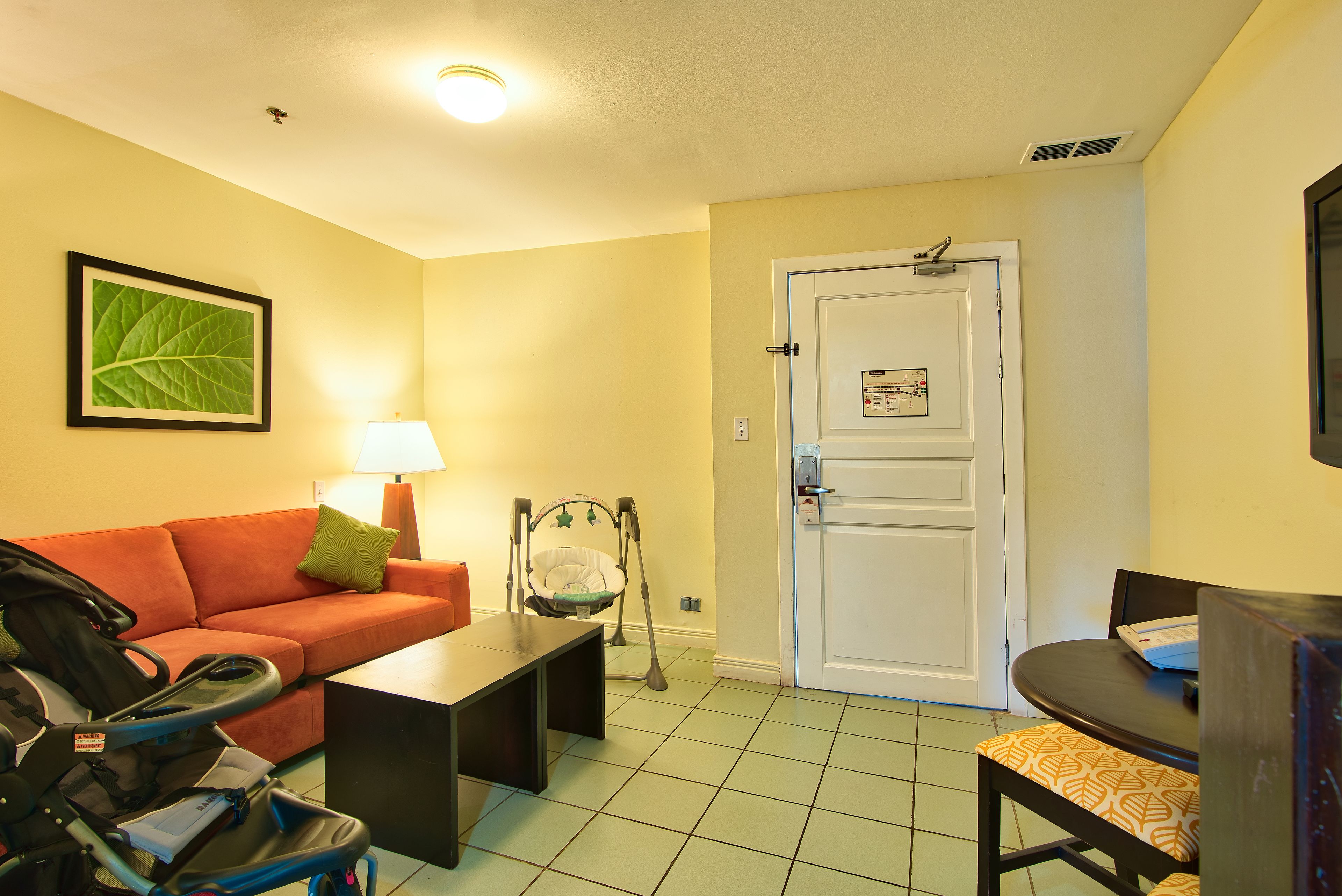 Un salon avec un canapé, une table basse, une poussette, une porte avec une serrure et un tableau encadré accroché au mur.