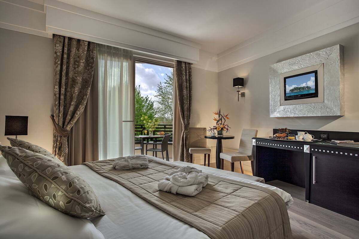 A hotel room with a bed, a desk, a chair, a TV mounted on the wall, and a view of the outdoors.