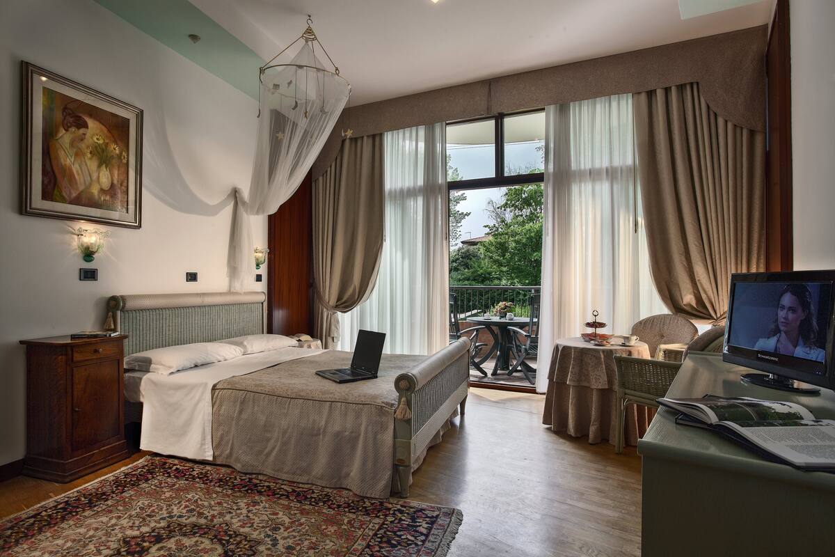 A bedroom with a bed, a laptop, a television, and a balcony with a table and chairs.