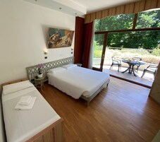 Habitación de hotel con una cama grande, una mesita con una planta en maceta y vistas al exterior a través de una puerta corrediza de vidrio.