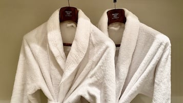 Two white bathrobes hanging on wooden hangers.
