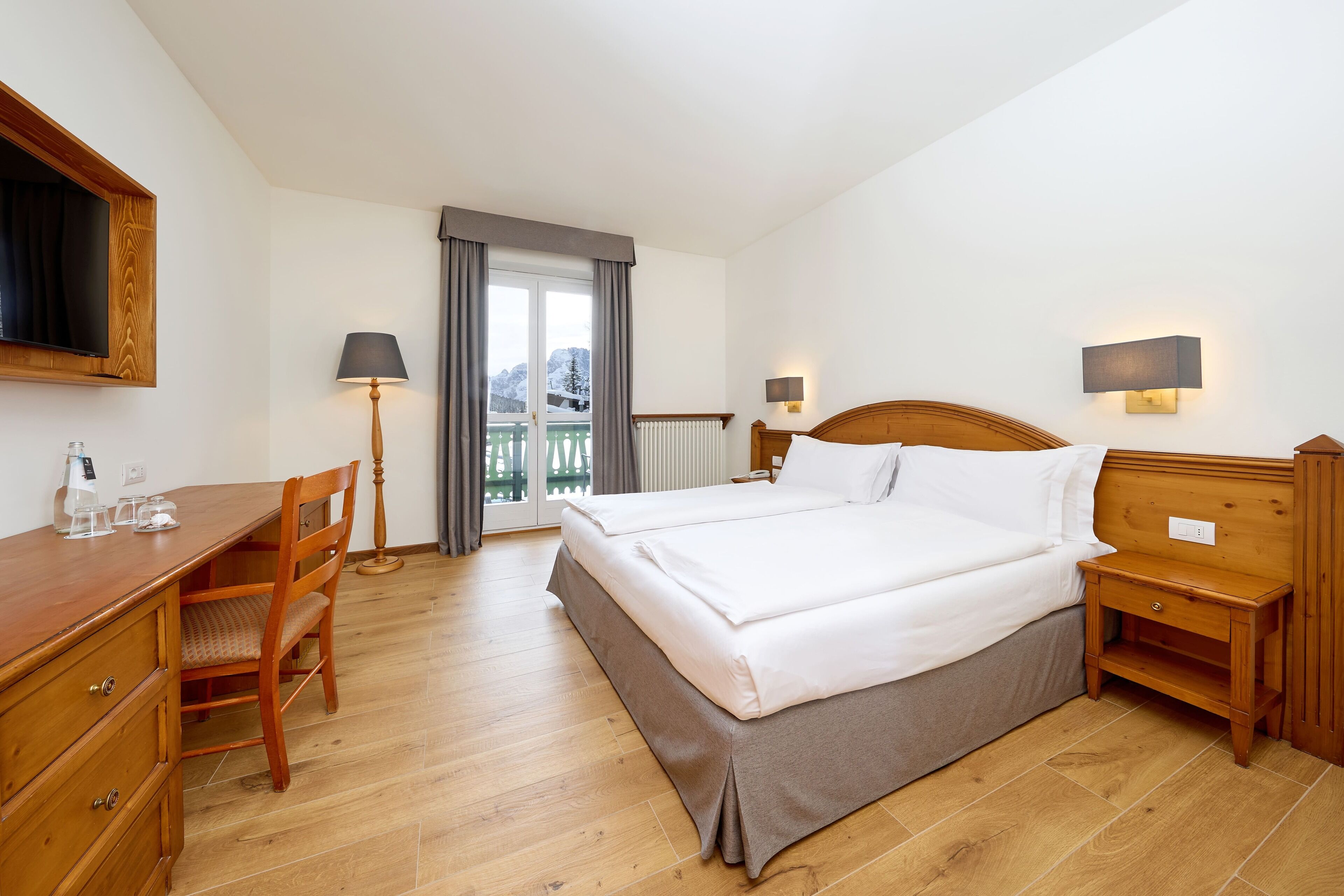 A hotel room with a wooden desk, two beds, a chair, and a view of the outdoors.