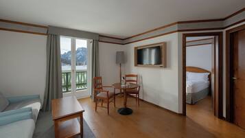 Una camera d'albergo con pavimento in legno, un divano, un tavolo, una televisione e un letto.