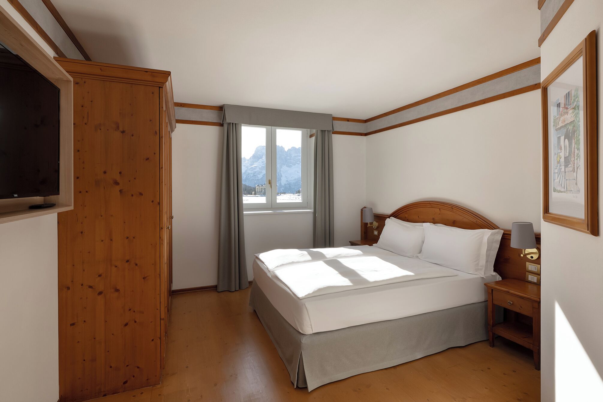 A bedroom with a bed, a nightstand, a TV, and a window with curtains.