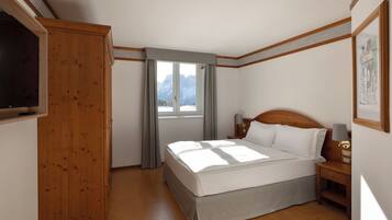 A bedroom with a bed, a nightstand, a TV, and a window with curtains.