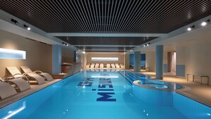 Piscina interior moderna com espreguiçadeiras e design geométrico no teto.