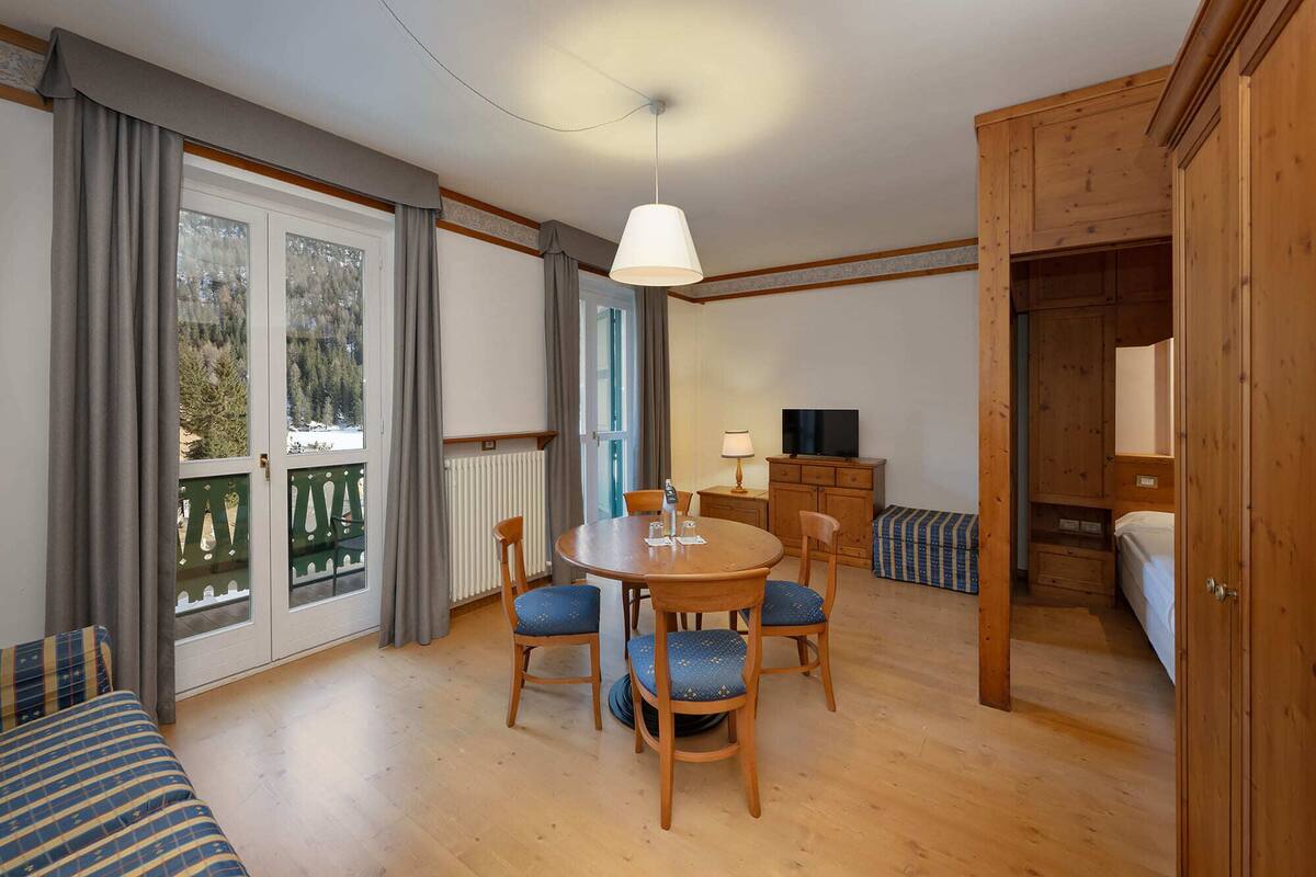 Une pièce chaleureuse avec une table à manger en bois, quatre chaises, un téléviseur et un lit.