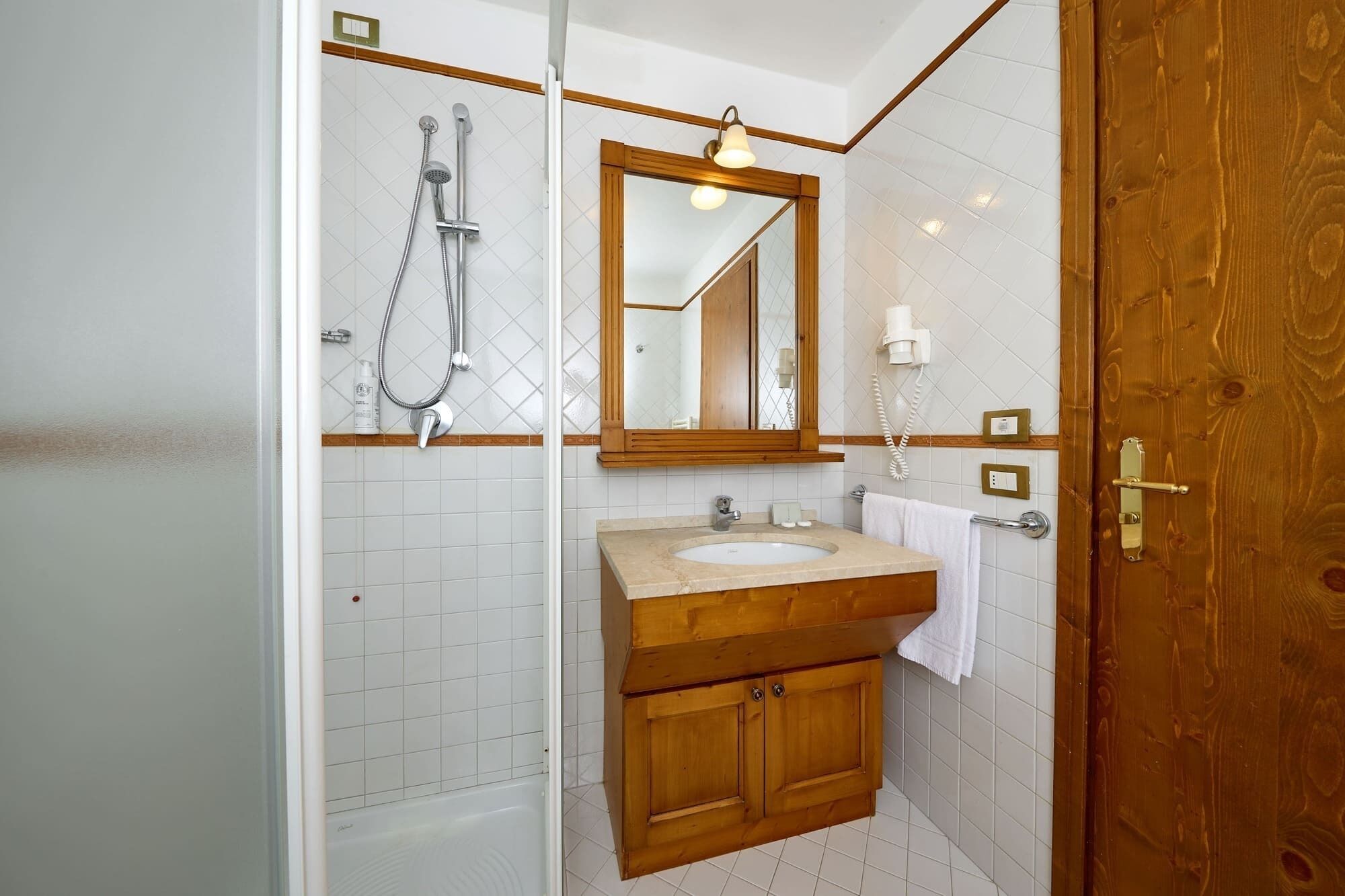 Un baño con tocador de madera, un espejo, ducha y una toalla colgada en la puerta.