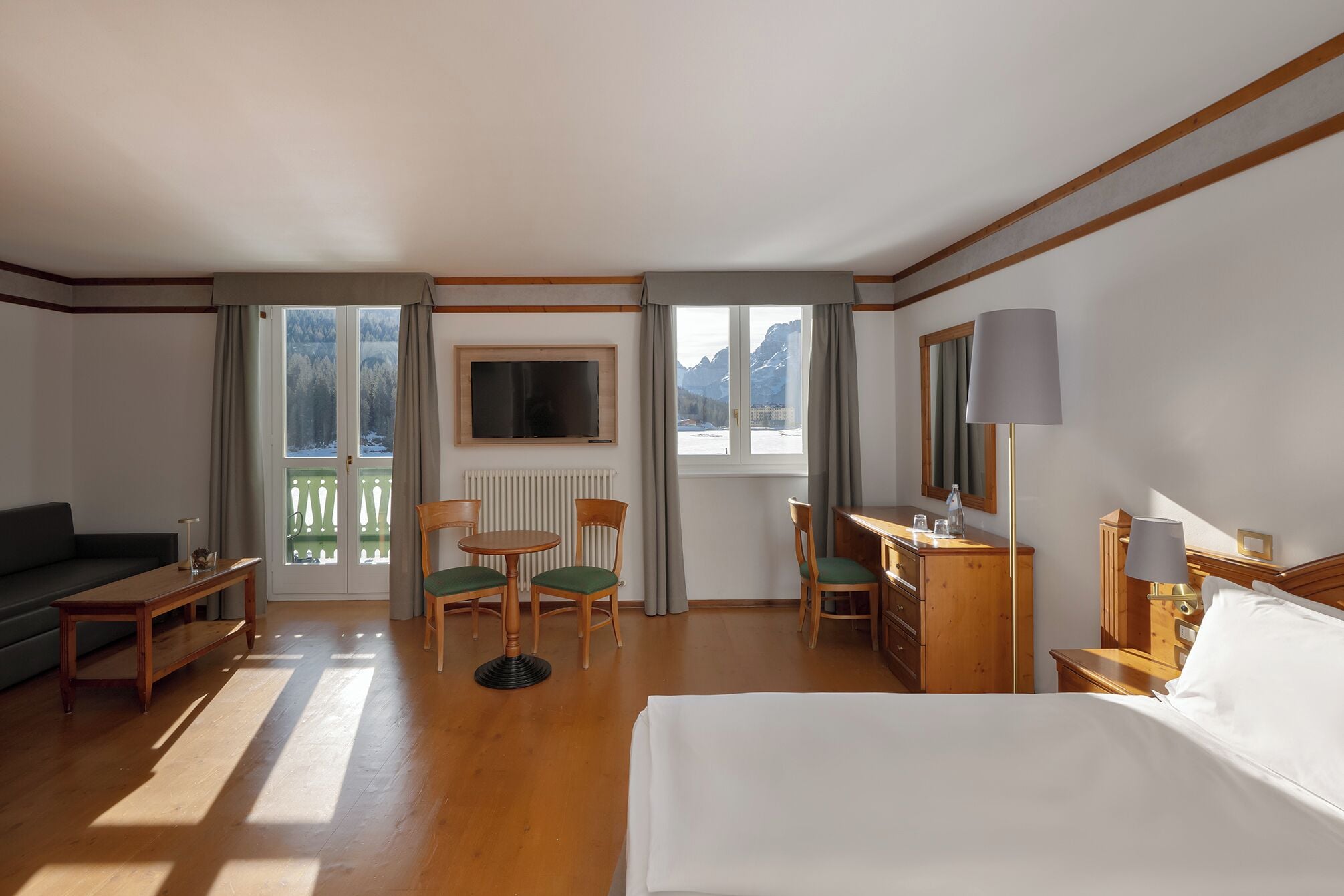 Ein Hotelzimmer mit einem Bett, einem Schreibtisch, zwei Stühlen, einem Sofa und Blick auf Berge durch die Fenster.