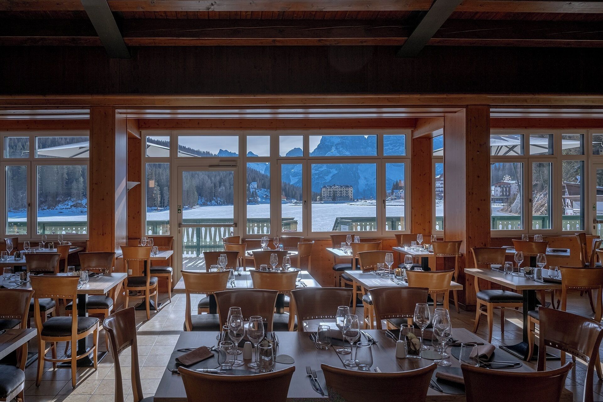 A restaurant with multiple tables and chairs, large windows offering a view of a snowy landscape and mountains.