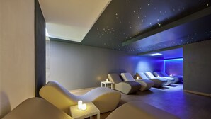 Uma sala de spa moderna com cadeiras reclináveis, uma pequena mesa com velas e um teto com projeções de estrelas.