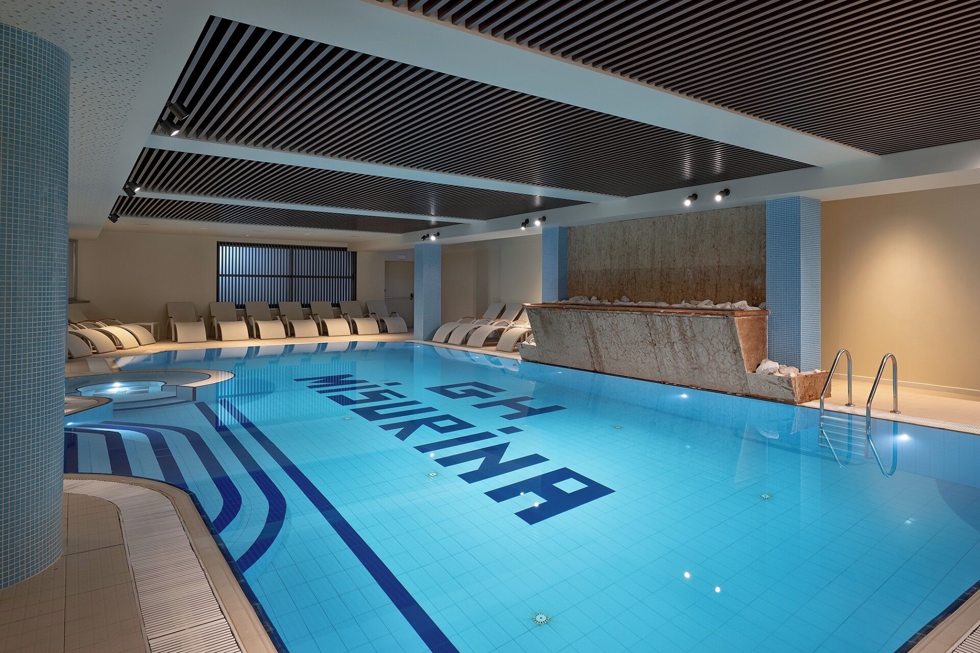 A swimming pool with lounge chairs and a stone wall.