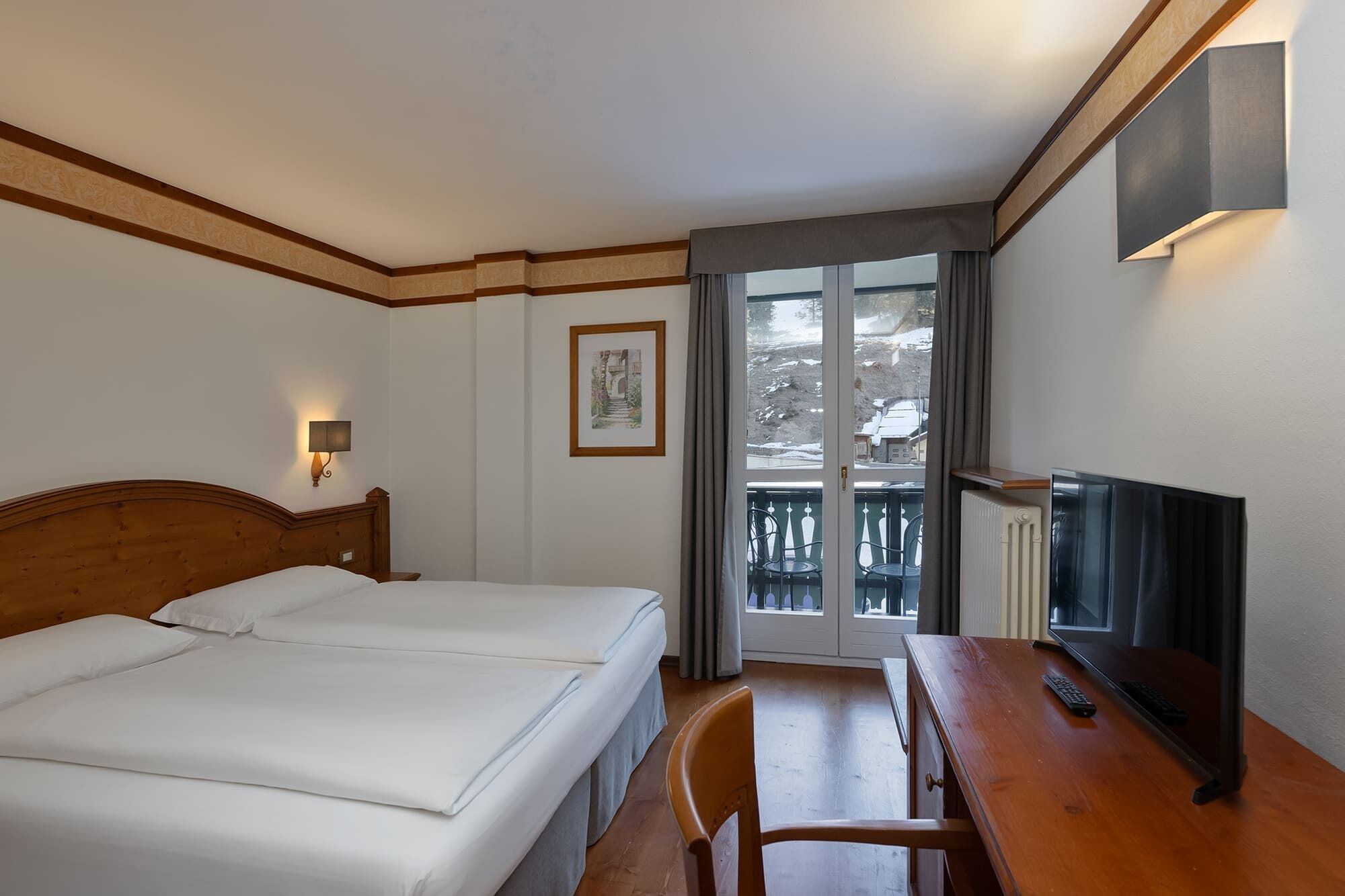 A hotel room with two beds, a desk with a TV, and a balcony with a view of the outside.