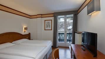 A hotel room with two beds, a desk with a TV, and a balcony with a view of the outside.