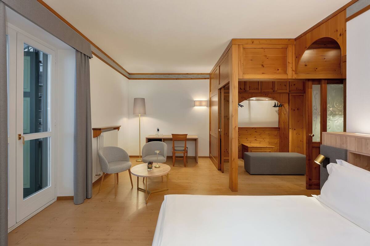 Une chambre d’hôtel avec un lit, un bureau, deux chaises, une lampe et une vue par la fenêtre.