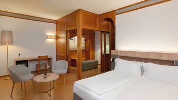 A hotel room with a bed, a desk, two chairs, a lamp, and a wardrobe.