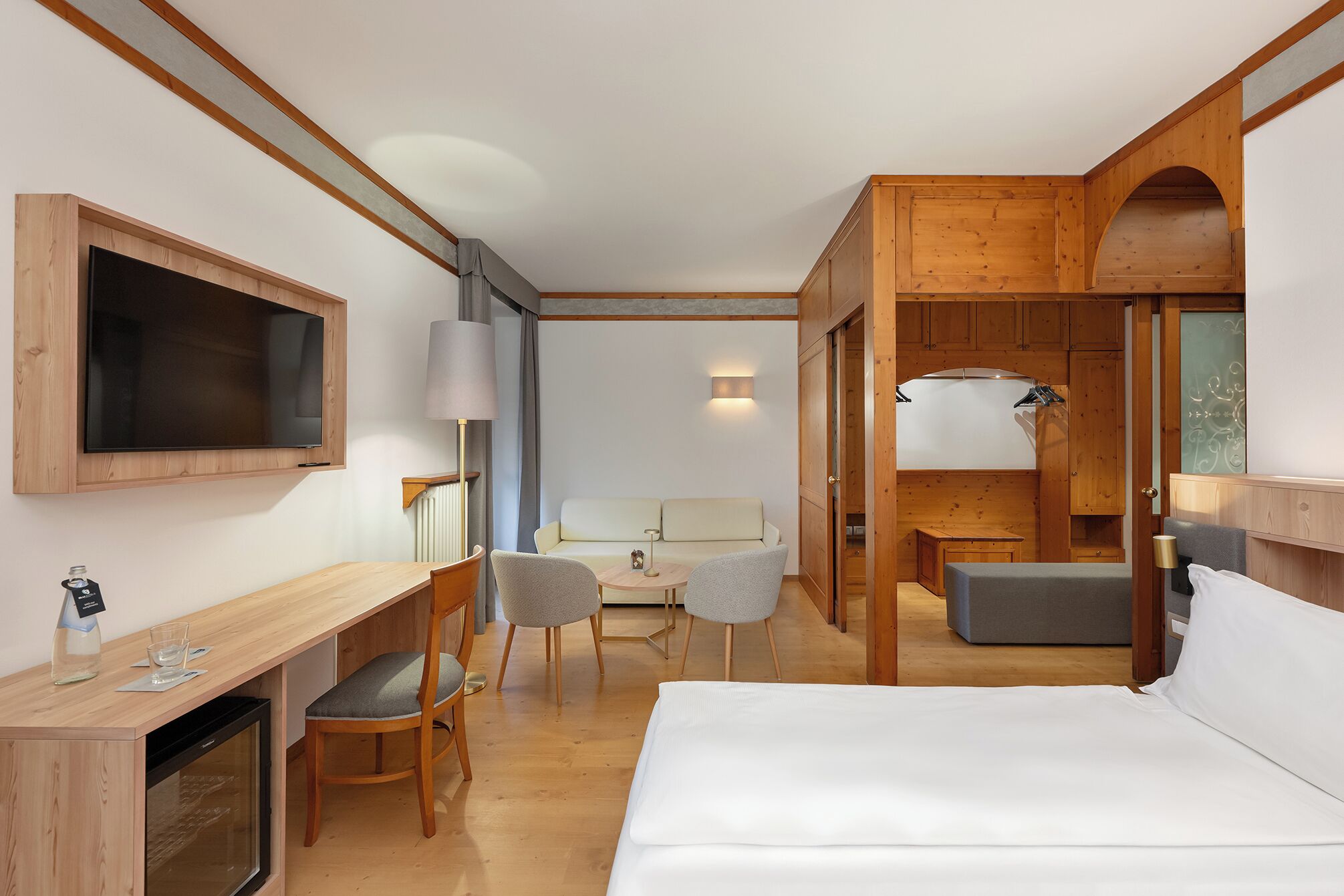Una camera d'albergo con un letto, una scrivania con una sedia, una televisione, una lampada e un divano.