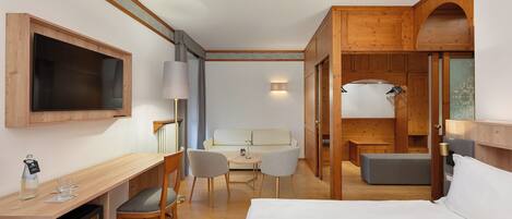 Una habitación de hotel con cama, escritorio con silla, televisión, lámpara y sofá.