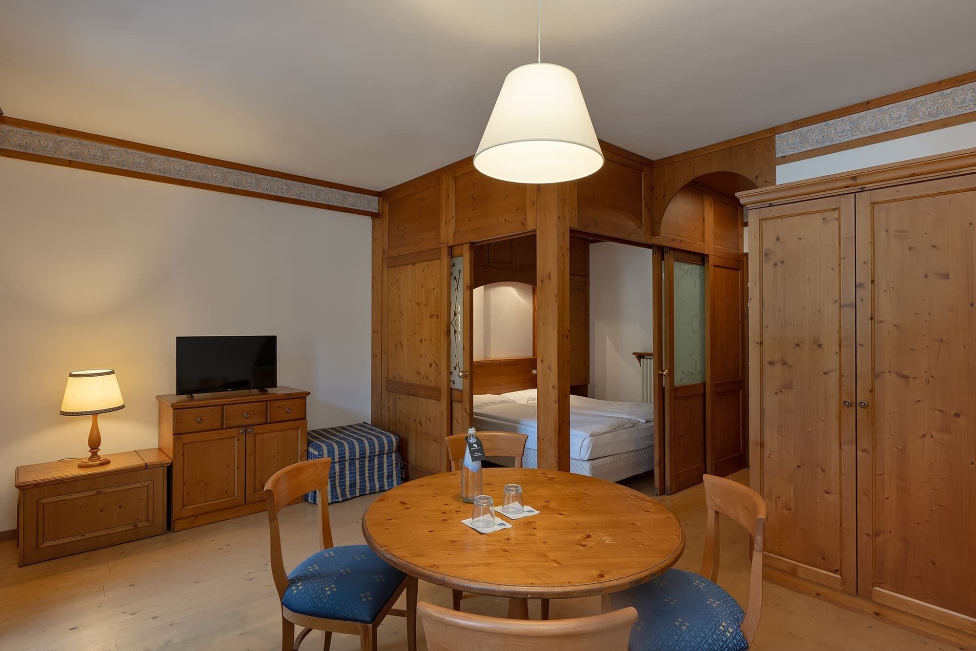 Ein Zimmer mit Holzboden, einem runden Tisch, Stühlen, einem Fernseher und einem Bett.